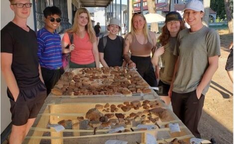 Seven students around a table with crockery and pottery from the archeological dig