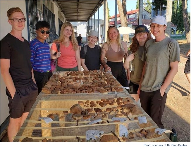 Seven students around a table with crockery and pottery from the archeological dig